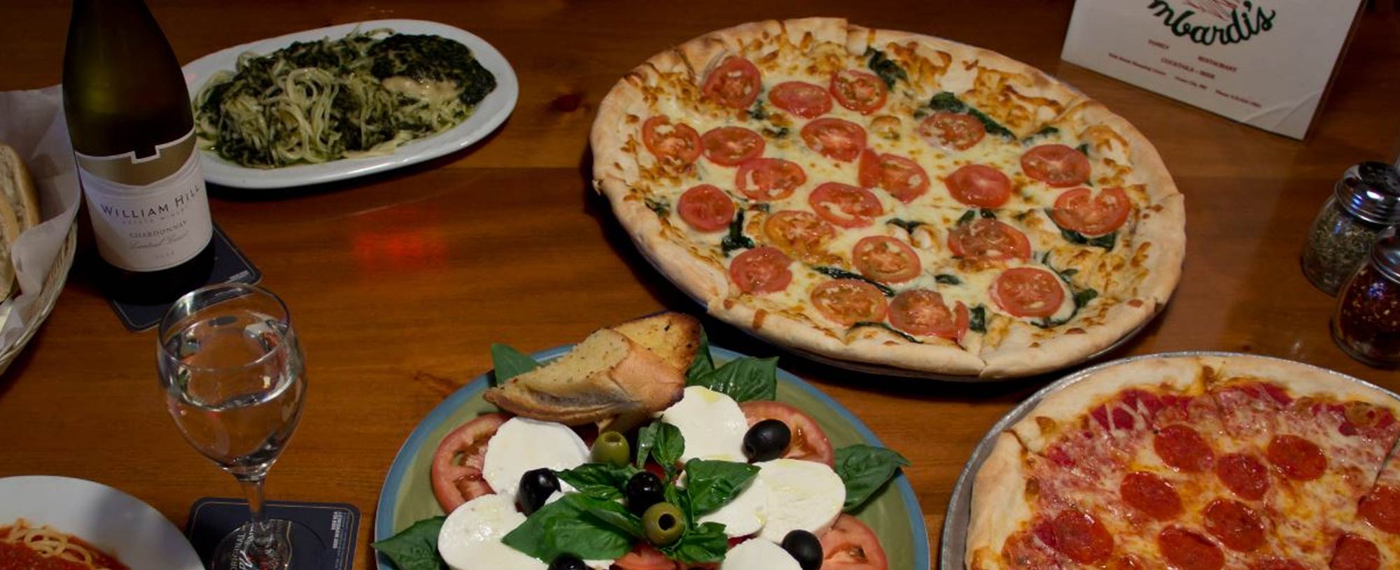 two pizzas, past and italian salad on table with wine at lombardi's pizza ocmd